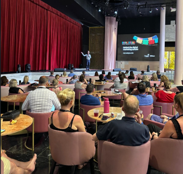 Man on stage presenting to a large group of peoplw image