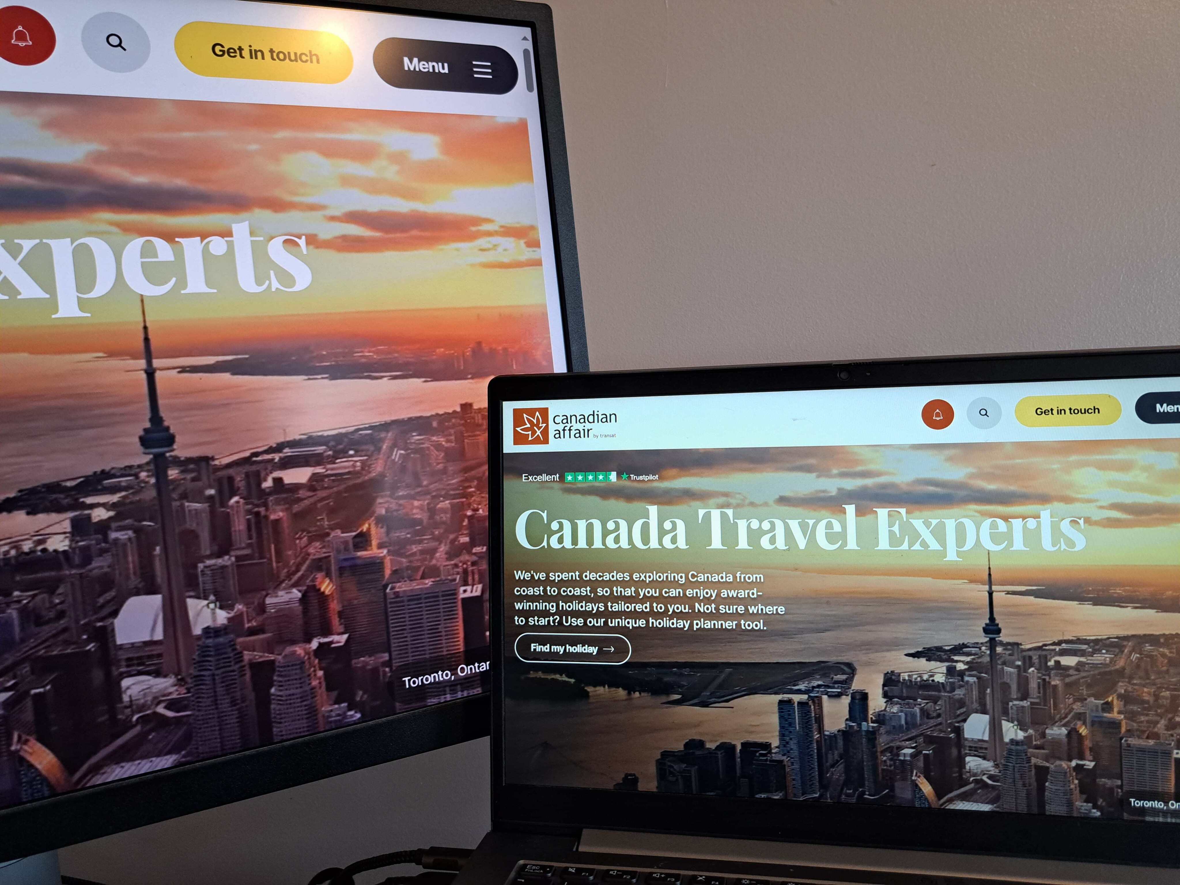 Image shows two screens, a desktop monitor and a laptop, both displaying the home page of the Canadian Affair travel website. The website features a large, scenic photograph of the Toronto skyline at sunset, with the CN Tower clearly visible against an orange and blue sky.  On the laptop screen, the text 